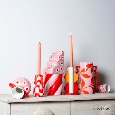 Conjunto de castiçais e jarros de cerâmica coloridos com velas cor de rosa em cima de cómoda clara