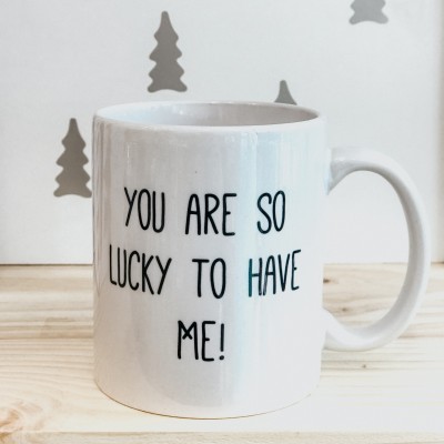 Caneca branca com texto preto sobre madeira clara e fundo com árvores cinzentas