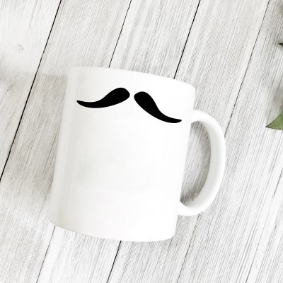 Caneca branca com desenho preto de bigode sobre superfície de madeira branca