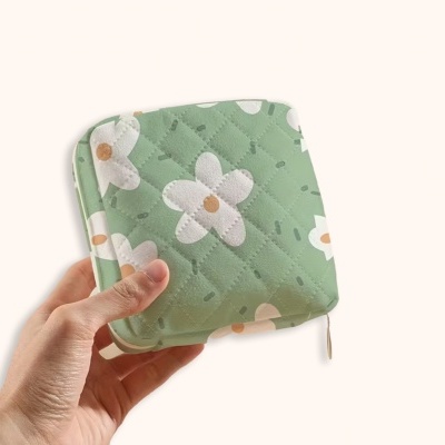 Carteira acolchoada verde com flores brancas e laranja, segurada por uma mão