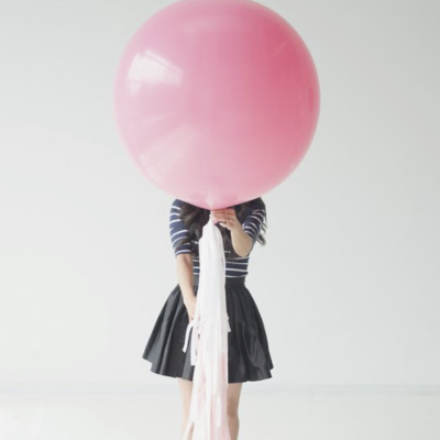 Mulher segurando balão rosa grande com fitas