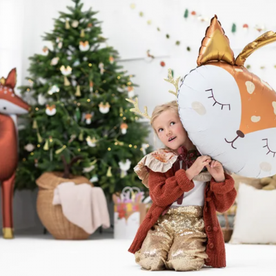 Boneco inflável de rena castanha e branco com criança ao lado, árvore de Natal ao fundo