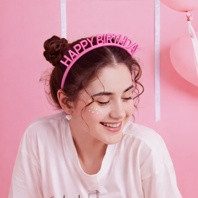 Pessoa sorridente com tiara rosa HAPPY BIRTHDAY e fundo rosa com balões