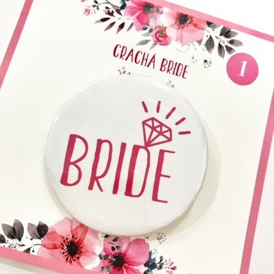 Crachá branco redondo com texto rosa BRIDE e desenho de diamante, em cartolina decorada com flores rosa