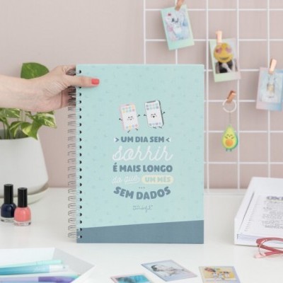 Caderno azul claro com texto, espiral e objetos de escritório ao fundo