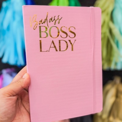 Caderno rosa com texto dourado e elástico