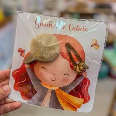 Conjunto de ganchos de cabelo com pompom bege e urso castanho em cartão ilustrado com menina de cabelo vermelho