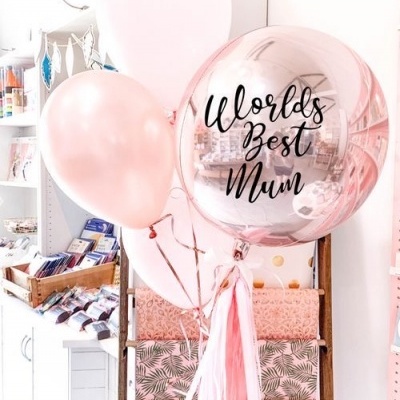 Balões cor-de-rosa e um balão metálico com texto preto numa loja de embrulho