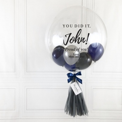 Balão transparente grande com balões coloridos no interior e texto de congratulação impresso