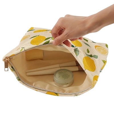 Necessaire branca com estampa de limões e fecho de correr aberto, mostrando pincéis e pote de creme dentro.