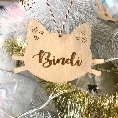 Enfeite de Natal de madeira em forma de gato pendurado numa árvore branca com decoração dourada e bola prateada