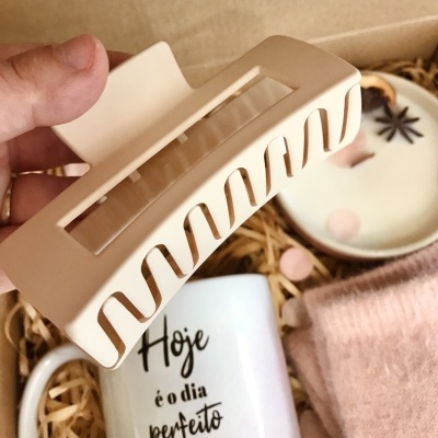 Presilha de cabelo bege e dourada segurada à frente de uma caneca branca e outros artigos em papel reciclado