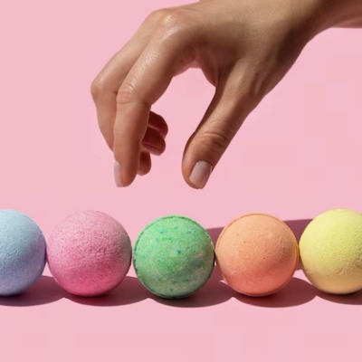 Sete bolas coloridas em linha e uma mão a segurar uma bola, fundo rosa