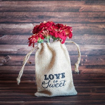 Saco de tecido com flores vermelhas e rosa em fundo de madeira escura