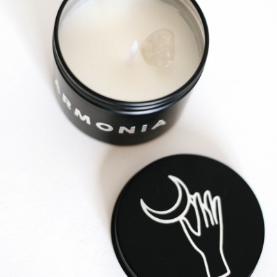 Vela branca em recipiente preto com tampa decorada com mão e lua