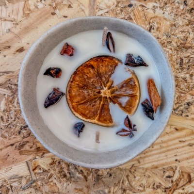 Vela branca numa taça cinzenta clara com decoração seca de laranja e especiarias sobre madeira