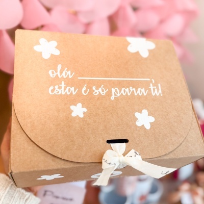 Caixa castanha com texto de boas-vindas e decoração de flores brancas.
