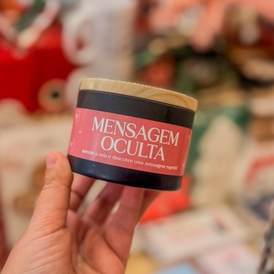 Vela preta com tampa de madeira e etiqueta vermelha com texto 'MENSAGEM OCULTA'