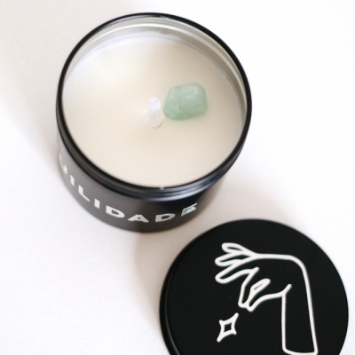 Vela branca em recipiente preto com tampa e desenho de mão