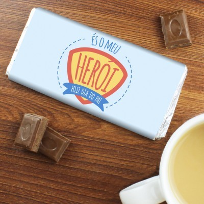 Barra de chocolate embrulhada com texto de Dia do Pai sobre mesa de madeira com pedaços de chocolate e chávena.