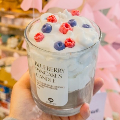 Vela decorativa com aparência de panquecas e frutos vermelhos em frasco de vidro