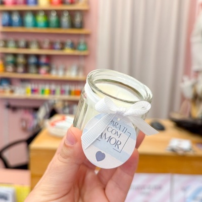 Vela branca em frasco de vidro com etiqueta e laço branco