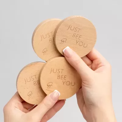 Porta-copos redondos de madeira clara gravados com texto e desenho de abelha