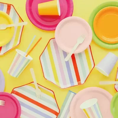 Pratos descartáveis coloridos com copos e garfos sobre fundo amarelo