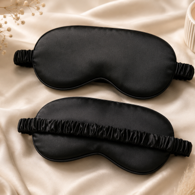 Máscaras de dormir pretas sobre tecido de cetim bege com vela e flores secas