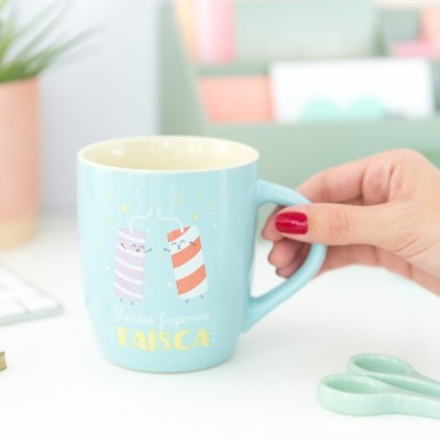 Caneca azul clara com desenho de palitos de fósforo e texto em português na mesa branca