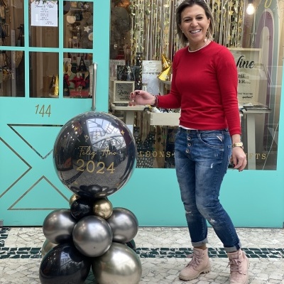 Balões decorativos em frente à porta de loja com mulher ao lado