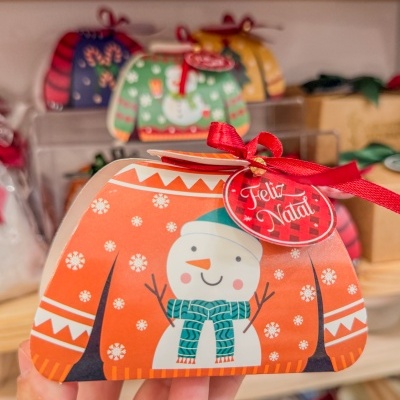 Embalagem de presente em forma de camisola com boneco de neve e etiqueta que diz Feliz Natal