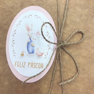 Etiqueta oval de Páscoa com coelho, pintainho, pato e texto 'FELIZ PÁSCOA', amarrada a presente em papel kraft