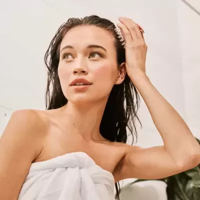 Mulher com toalha branca e cabelo molhado num ambiente com plantas e paredes brancas