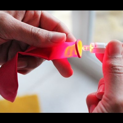 Mãos seguram balão vermelho com agulha inserida