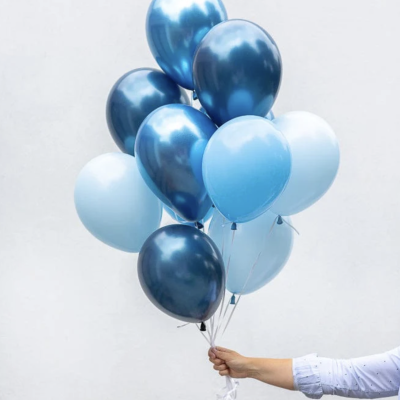 Balões em vários tons de azul, metalizados e opacos, segurados por uma mão com camisa branca