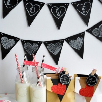 Decorações de festa com bandeirolas pretas e corações, garrafas de leite com canudos, sacos decorados com corações vermelhos.