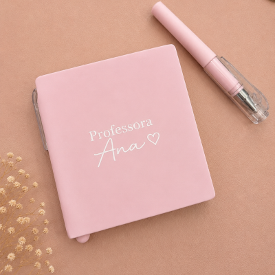 Caderno rosa Professora Ana e caneta rosa sobre superfície castanha clara