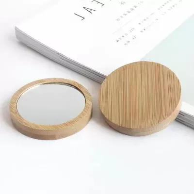 Espelho redondo pequeno com armação em madeira e tampa ao lado de livro aberto