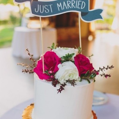 Bolo branco decorado com flores vermelhas e brancas e sinal azul com texto JUST MARRIED