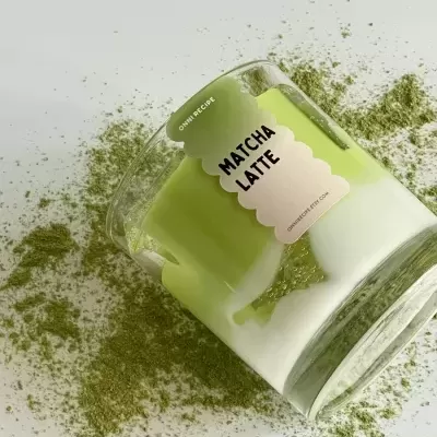vela perfumada matcha latte em vidro transparente com pó verde ao redor