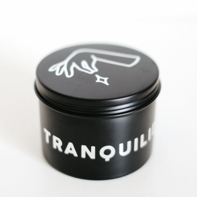 Frasco preto cilíndrico com ilustração branca na tampa e texto 'TRANQUIL' no corpo.