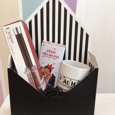 Conjunto de presente com caneta, chocolate e caneca dentro de caixa preta com riscas interiores