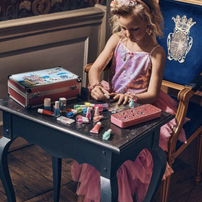 Menina a brincar com tubos coloridos em mesa preta, sentada em cadeira azul com brasão.