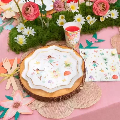 Conjunto de festa infantil com pratos e copo decorados e talheres de madeira em mesa rosa com flores artificiais