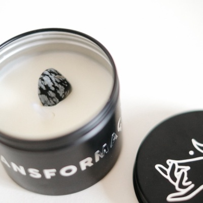 Vela branca em recipiente preto com tampa preta decorada com uma mão e uma lua brancas