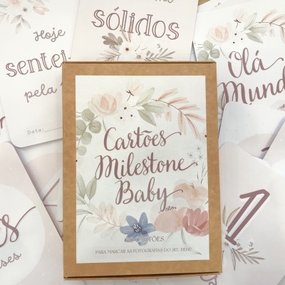 Conjunto de Cartões Milestone Baby decorados com flores e texto em tons pastel, empilhados sobre uma mesa de madeira clara