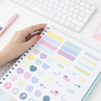 Caderno espiral com autocolantes coloridos em mesa branca com teclado e canetas