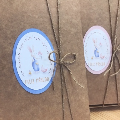 Caixas de papelão castanho com etiquetas de coelho e texto Feliz Páscoa, amarradas com corda em fundo de madeira clara