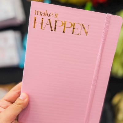 Caderno rosa com capa rígida e texto dourado make it HAPPEN